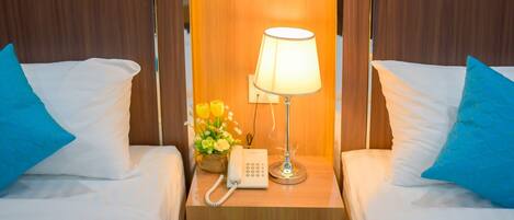 Habitación de hotel con dos camas, una mesita de noche con lámpara, teléfono y un jarrón con flores.