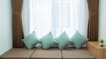 A room with a window seat, brown curtains, and a small plant on a wooden side table.