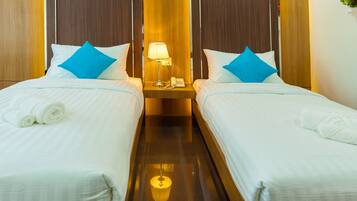 A hotel room with two beds, each with white linens and blue pillows, a bedside table with a lamp and phone, and a wooden headboard.