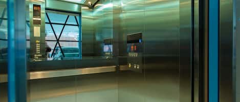 An elevator interior with metallic walls, a glass door, and a digital display showing floor numbers.