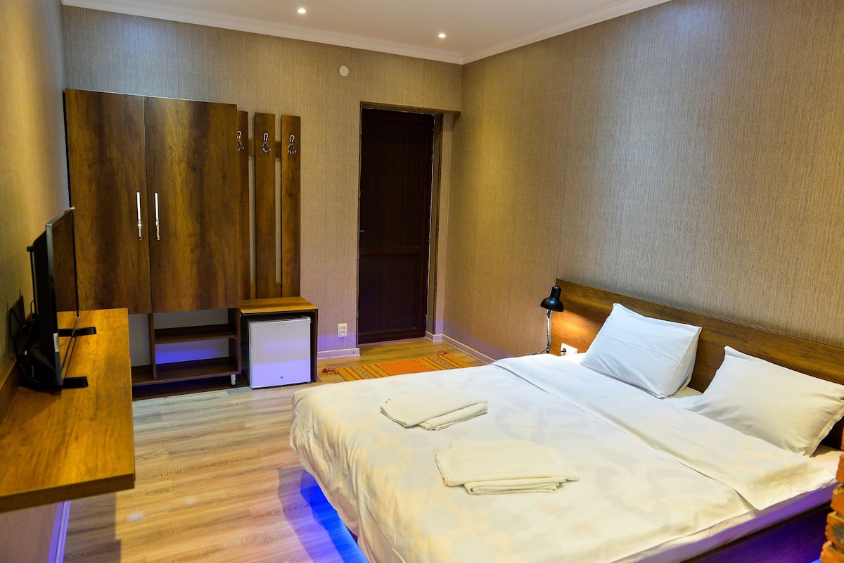 A hotel room with a bed, bedside table, TV, wardrobe, and a small desk.