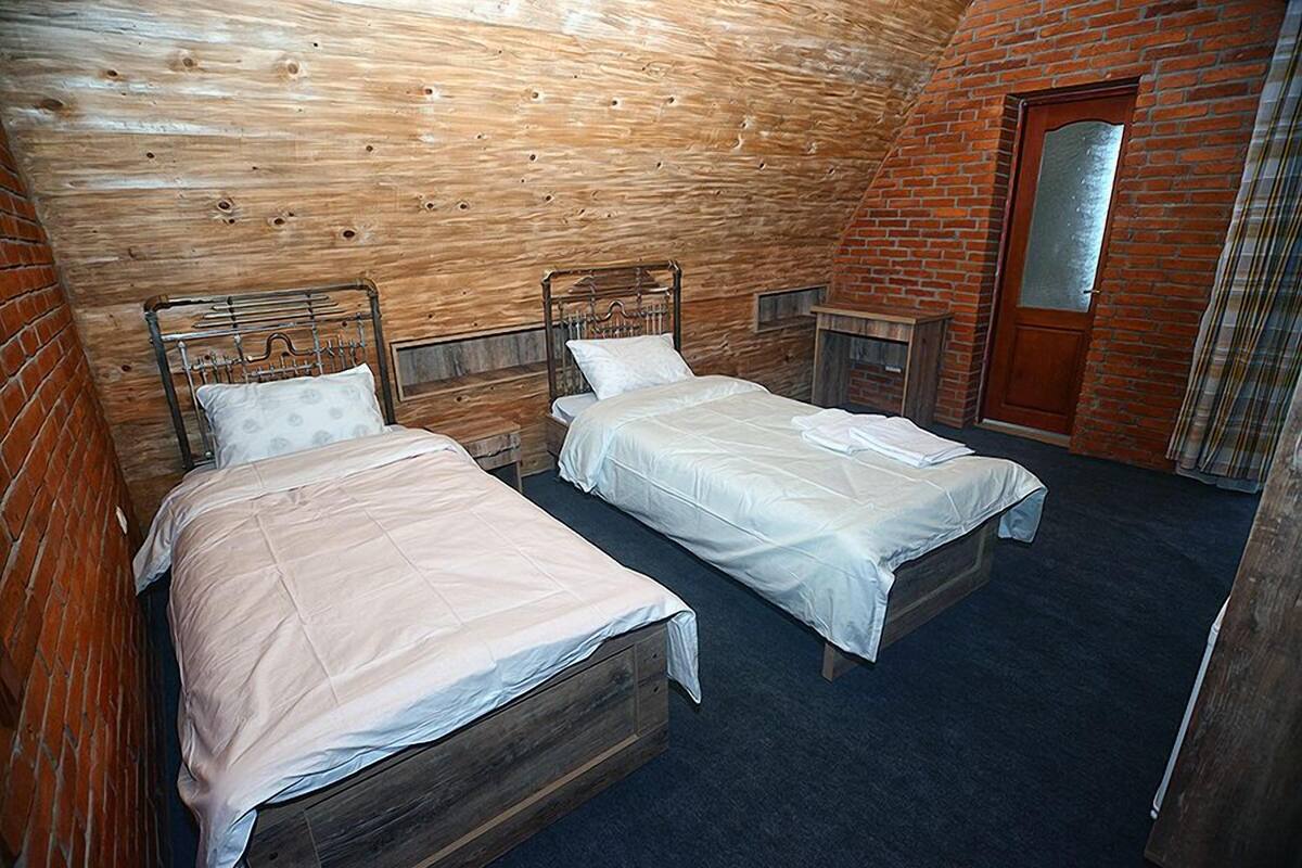 A room with two wooden beds, a brick wall, a wooden ceiling, and a door.