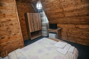 A wooden cabin bedroom with a bed, a desk, and a television.