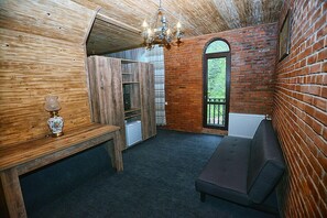 A cozy room with a wooden ceiling, a bench, a small table with a lamp, a radiator, and a view through a window.