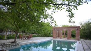 Piscina com estrutura de tijolo, cercada por um muro de pedra e vegetação.
