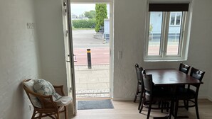 Una habitación amplia con comedor, un rincón de estar con sillas de mimbre y vistas a un espacio exterior a través de un vano.