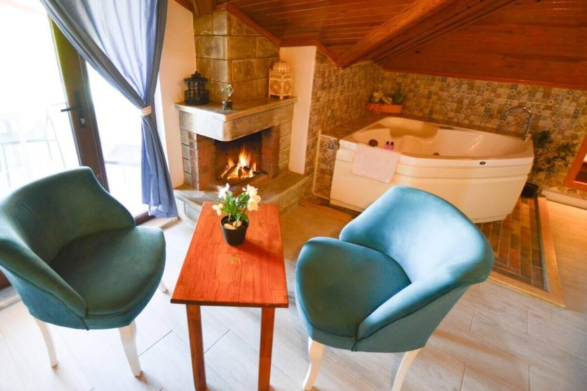 A cozy room with a fireplace, a large bathtub, and two teal armchairs.