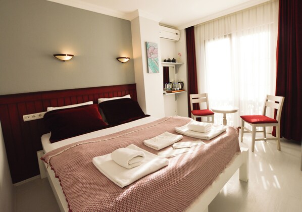 A neatly made bed with white and red linens, a bedside table, a chair, and a window with curtains.