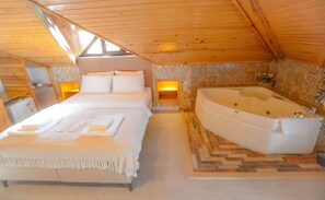 A bedroom with a large bed, a built-in bathtub, and a stone wall.