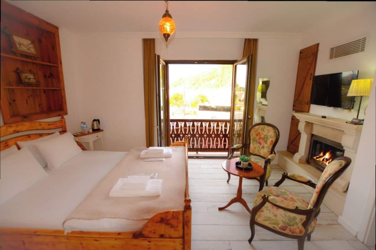 A hotel room with a bed, a chair, a fireplace, and a TV.