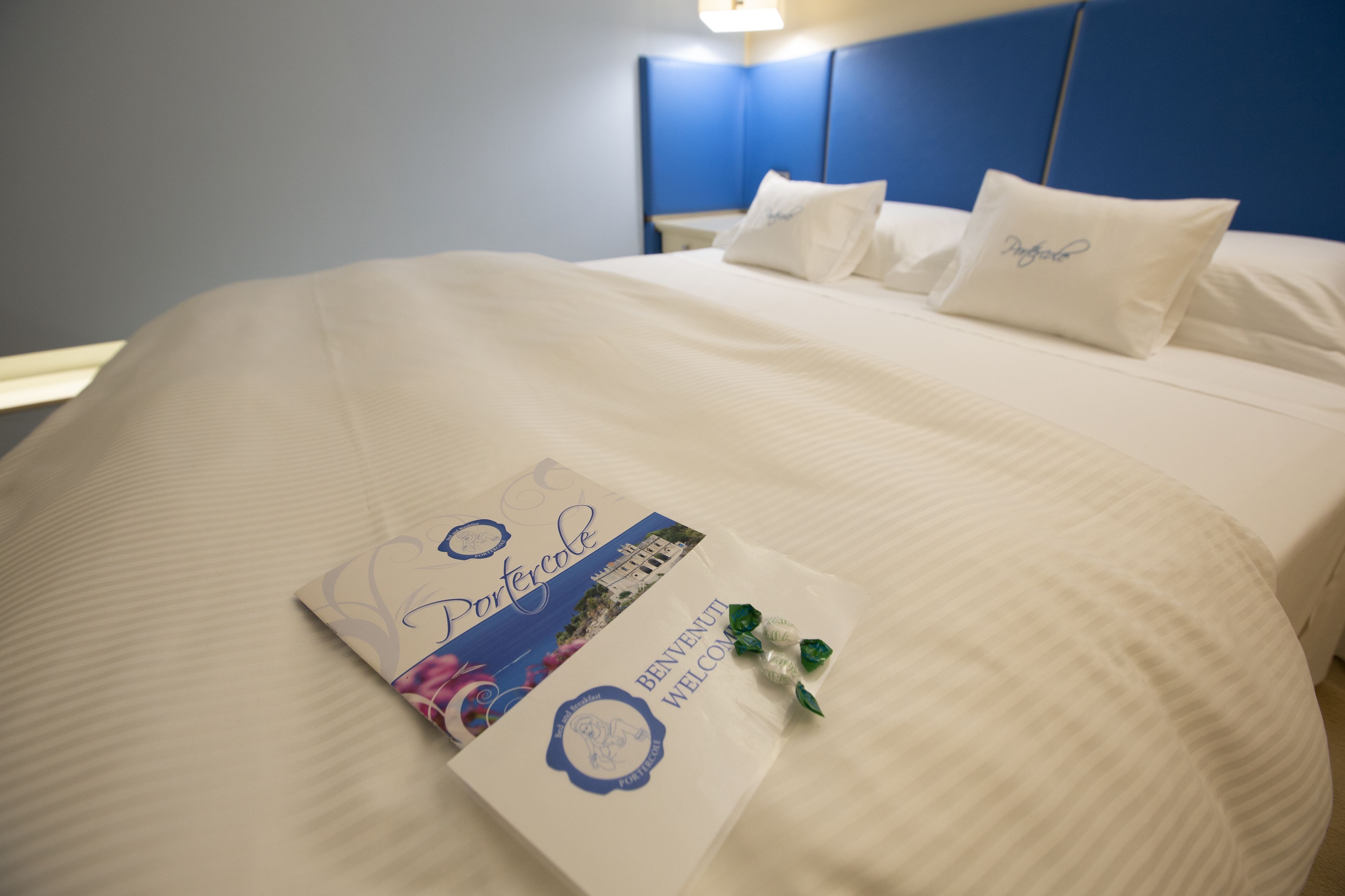 A neatly made bed with a welcome mat and a brochure, a nightstand with a lamp, and a blue headboard.
