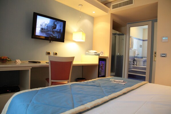 A hotel room with a bed, a desk, a chair, a television, and a bathroom visible through an open door.