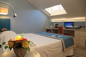 A bedroom with a bed, a desk, a computer, and a skylight.