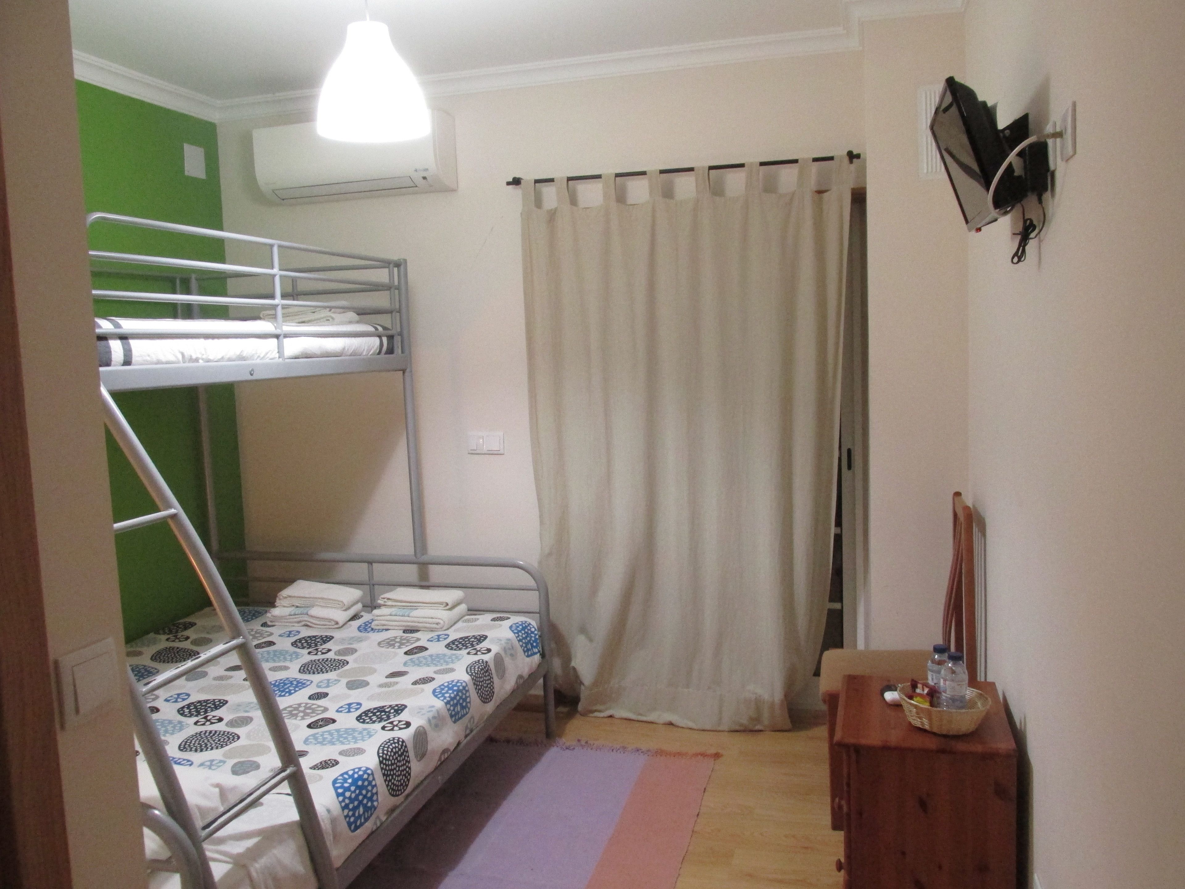 Une chambre avec des lits superposés, un rideau, une petite table avec un panier et un appareil de climatisation.