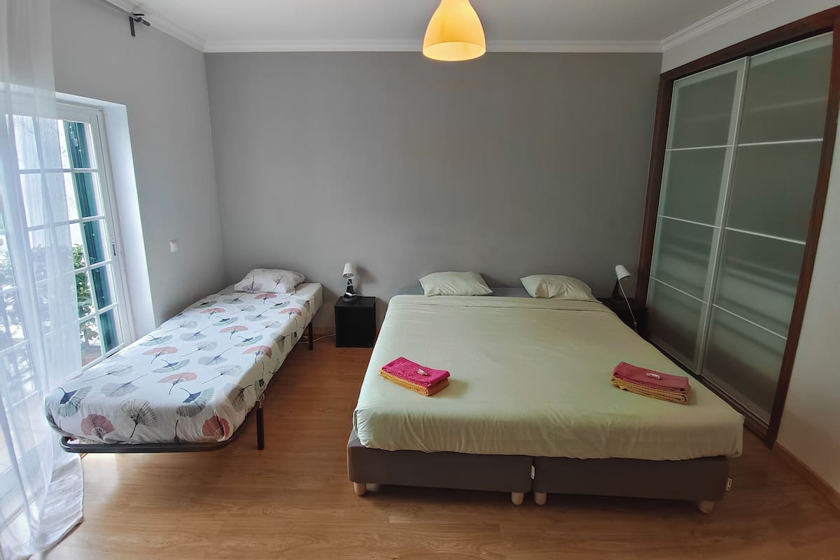 A bedroom with two beds, a window, and a hanging light fixture.