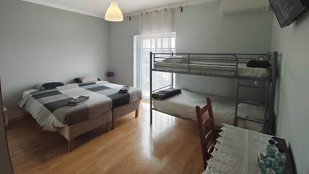 Habitación compacta con una litera, una cama individual y una pequeña mesa con botellas de agua.