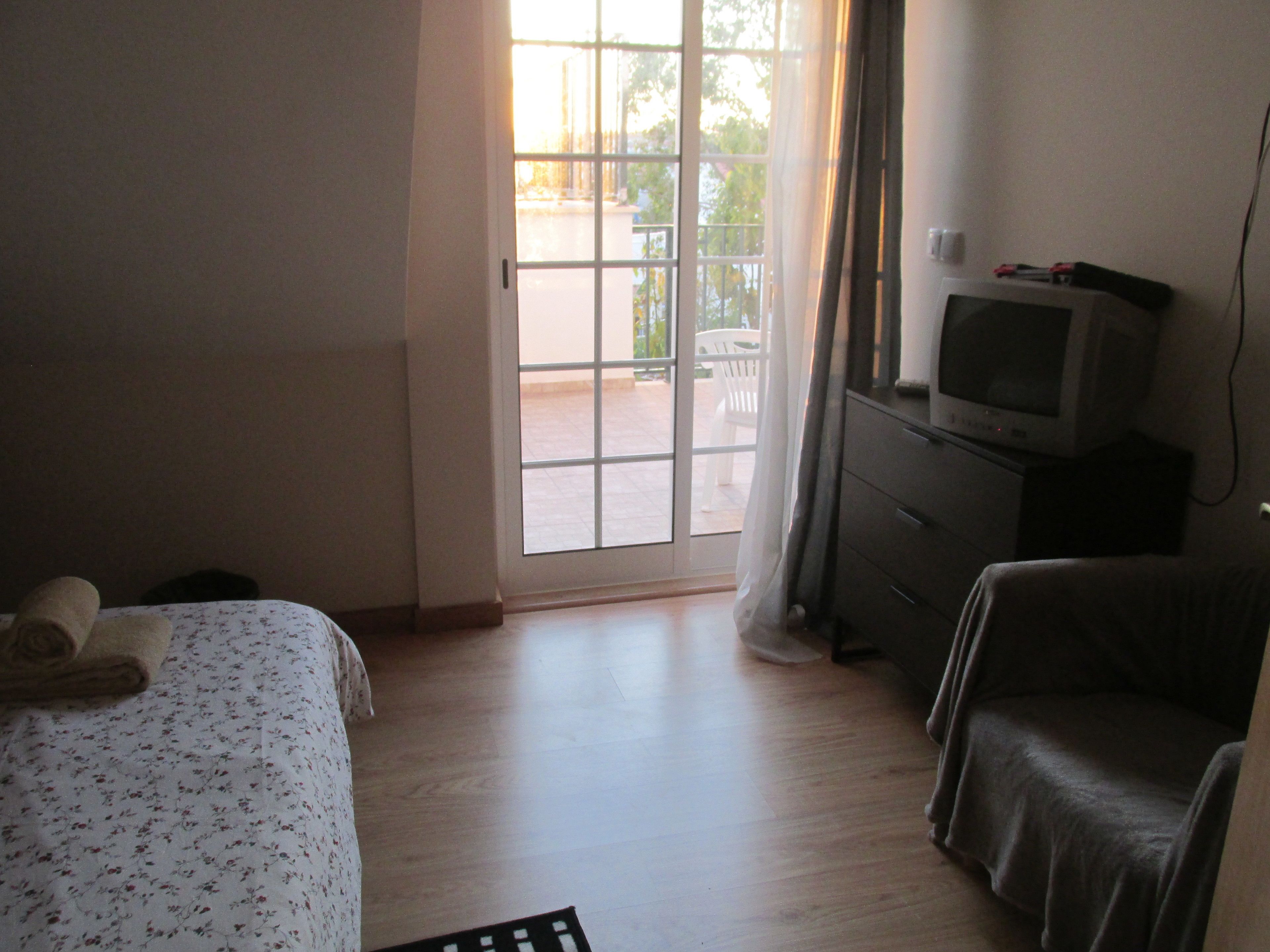 A hotel room with a bed, a chair, a television on a dresser, and a sliding glass door leading to an outdoor area.