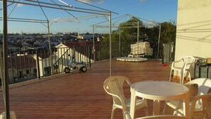 Un patio techado al aire libre con vistas a la ciudad, que incluye una mesa y sillas, un coche pequeño y un pabellón.