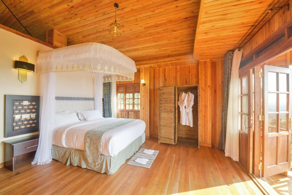 A wooden-paneled bedroom with a canopy bed, a bedside table, and a view of the outdoors.