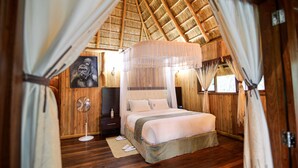 A bedroom with a bed, a bedside table, a fan, and a painting on the wall.