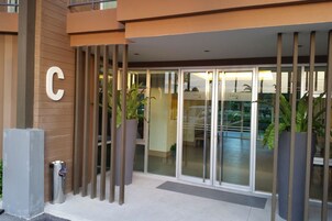 Una entrada de hotel moderna con un gran letrero en forma de 'C', puertas de cristal y plantas en macetas.