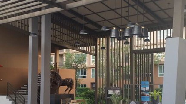 A covered outdoor seating area with wooden chairs and tables, a staircase, and a decorative horse statue. - The Relaxing Room Mountain View at Baan Tew Lom Condominium Cha Am - Hua Hin (Cha-am)