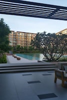 A poolside area with a view of a multi-story building, outdoor seating, and a pergola structure.