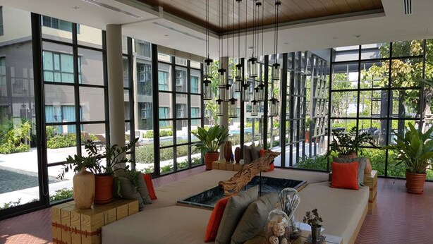 A spacious lobby with large windows, a central seating area with cushions and a coffee table, and potted plants.