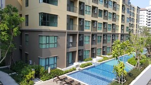 A modern apartment building with a swimming pool, balconies, and greenery.