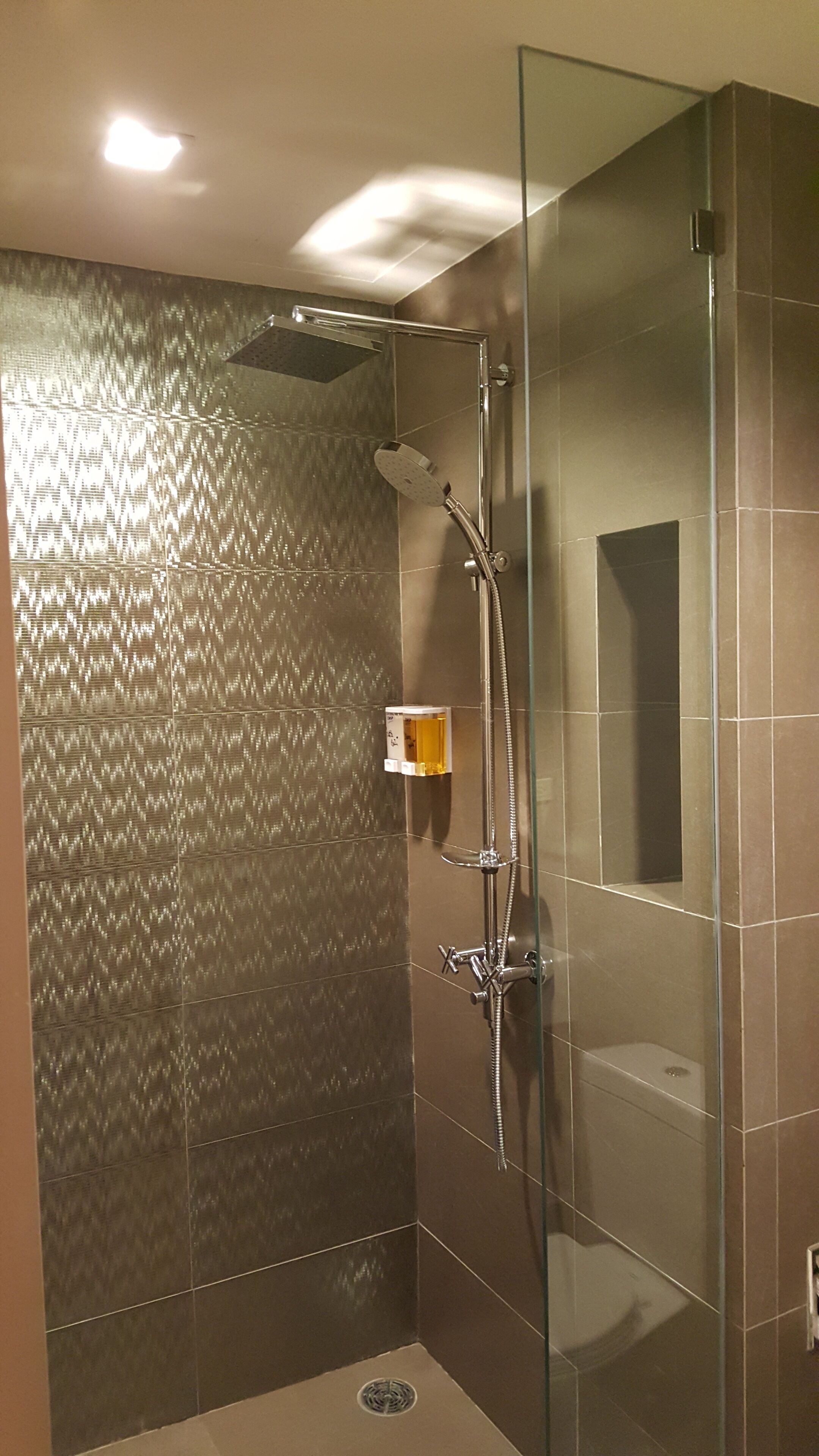 Un baño moderno con cabina de ducha de vidrio, ducha de mano y dispensador de jabón mural.