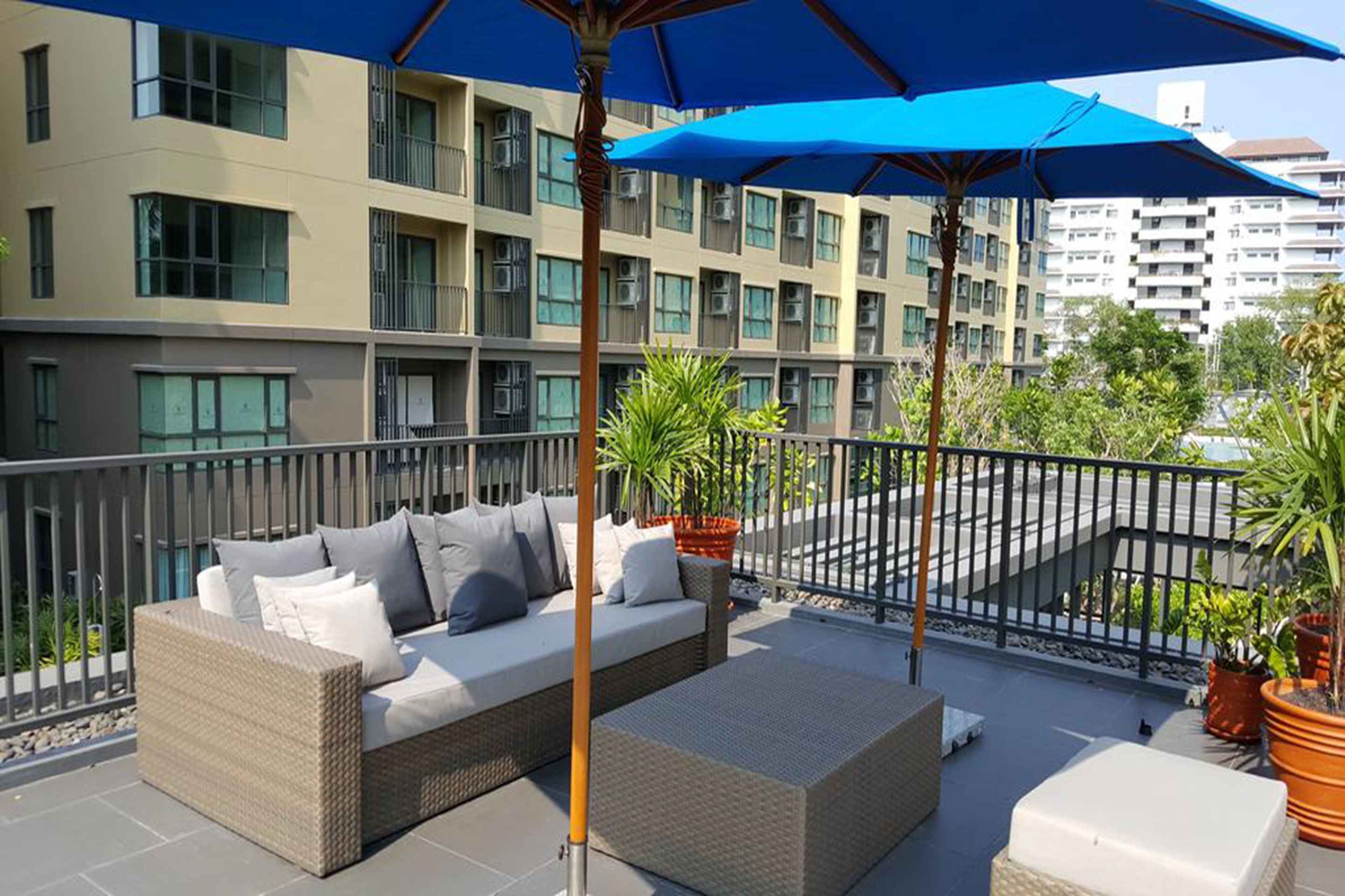 A balcony with a sofa, potted plants, and a blue umbrella.