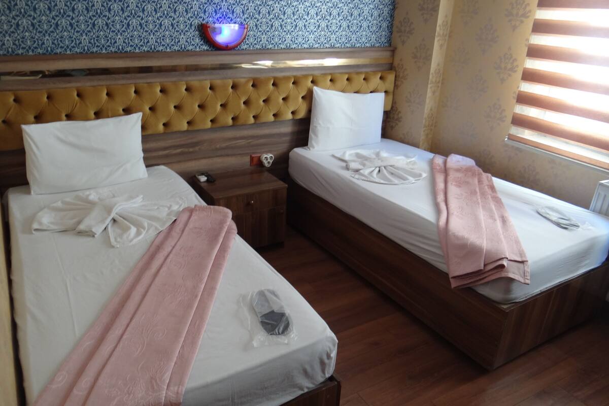 A hotel room with two beds, a wooden headboard, a nightstand, and a wall-mounted light fixture.