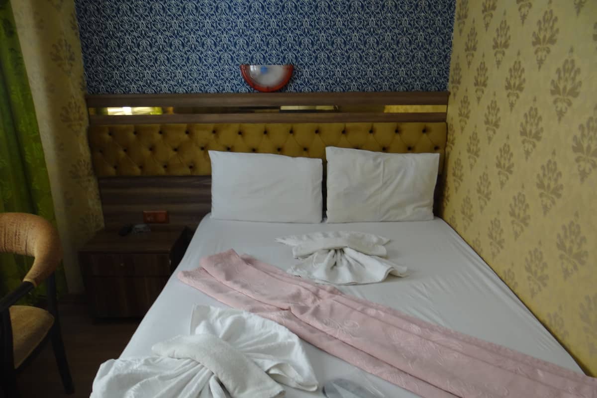 A hotel room with a bed, pillows, a bedside table, a chair, and a wall with patterned wallpaper.