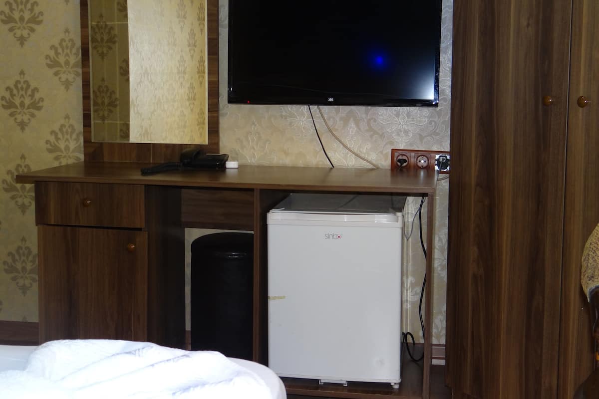 A hotel room with a bed, a desk with a flat-screen TV, a mirror, a refrigerator, and a telephone.