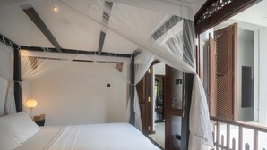 Un llit amb dosser, una nitòria amb una làmpada i vista al balcó exterior.