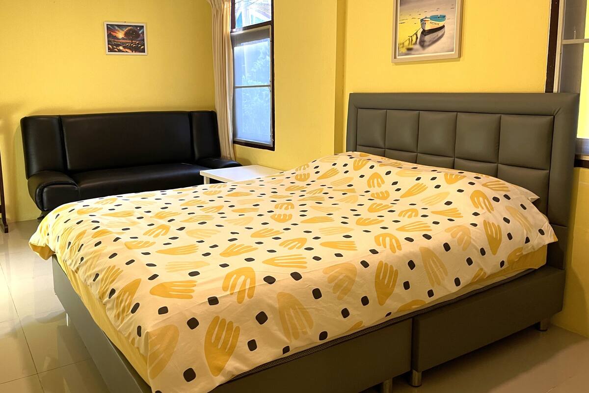 A bedroom with a bed, a sofa, a window, and a painting on the wall.