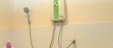 A bathroom with a shower unit mounted on the wall, a handheld showerhead, and a soap dispenser on a small shelf.
