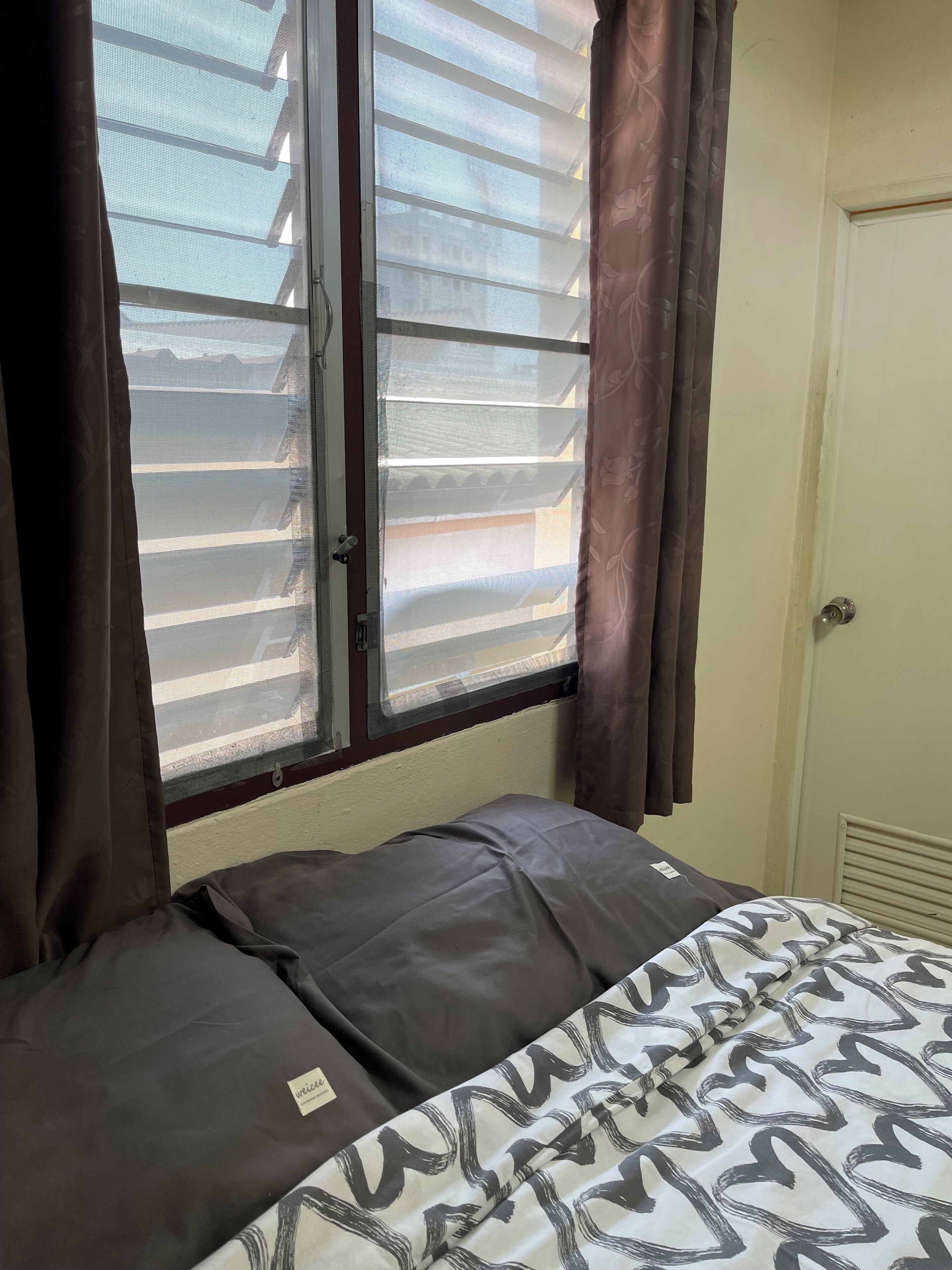 A bedroom with a bed, a window with blinds, and a door.