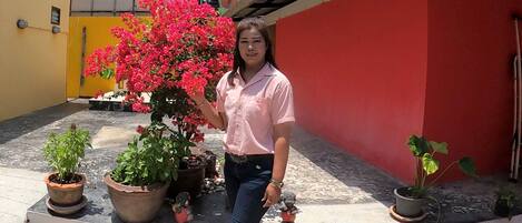 A woman standing in a courtyard with potted plants and a red wall.
