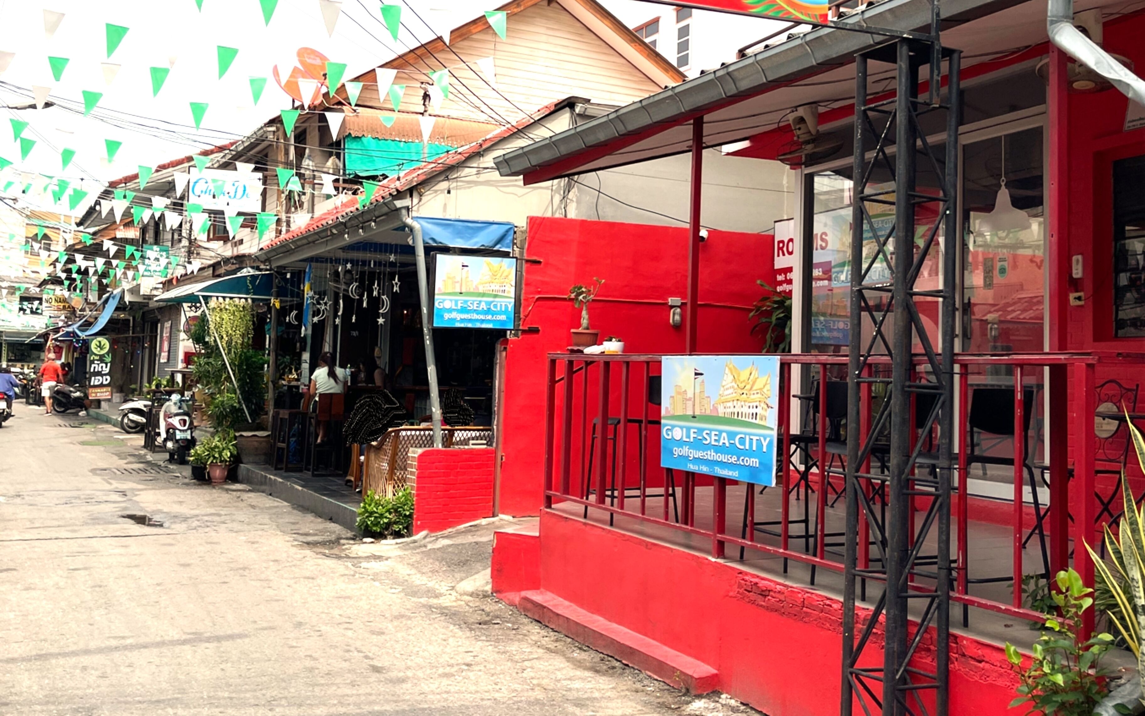 A red building with a sign for Golf-Sea-City. There are potted plants outside and a metal railing in front.