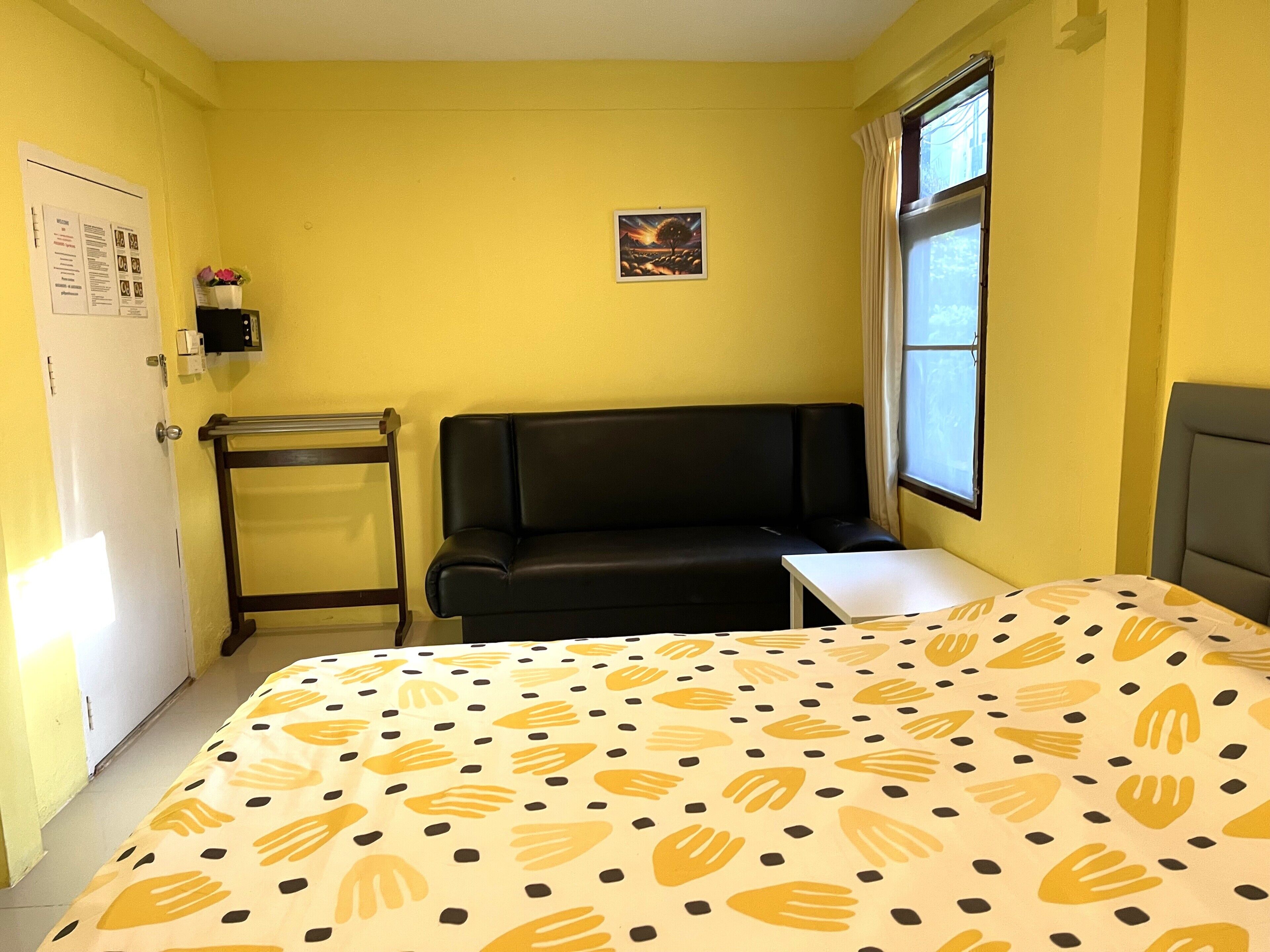 A room with a bed, a black sofa, a small table, a window, and a wall-mounted shelf with a picture.