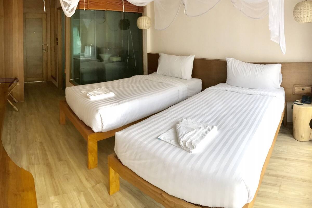 Habitación de hotel con dos camas, televisión y baño visible a través de una puerta de cristal.