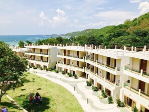 A multi-story hotel with balconies overlooking a landscaped area and a view of the sea. - Sealey Resort Koh Larn (Koh Lan)