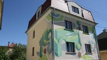 Un edifici de diverses plantes amb una façana singular de color verd i blanc, que destaca per una combinació d'obertures rectangulars i allargassades, i una xemeneia ben visible.