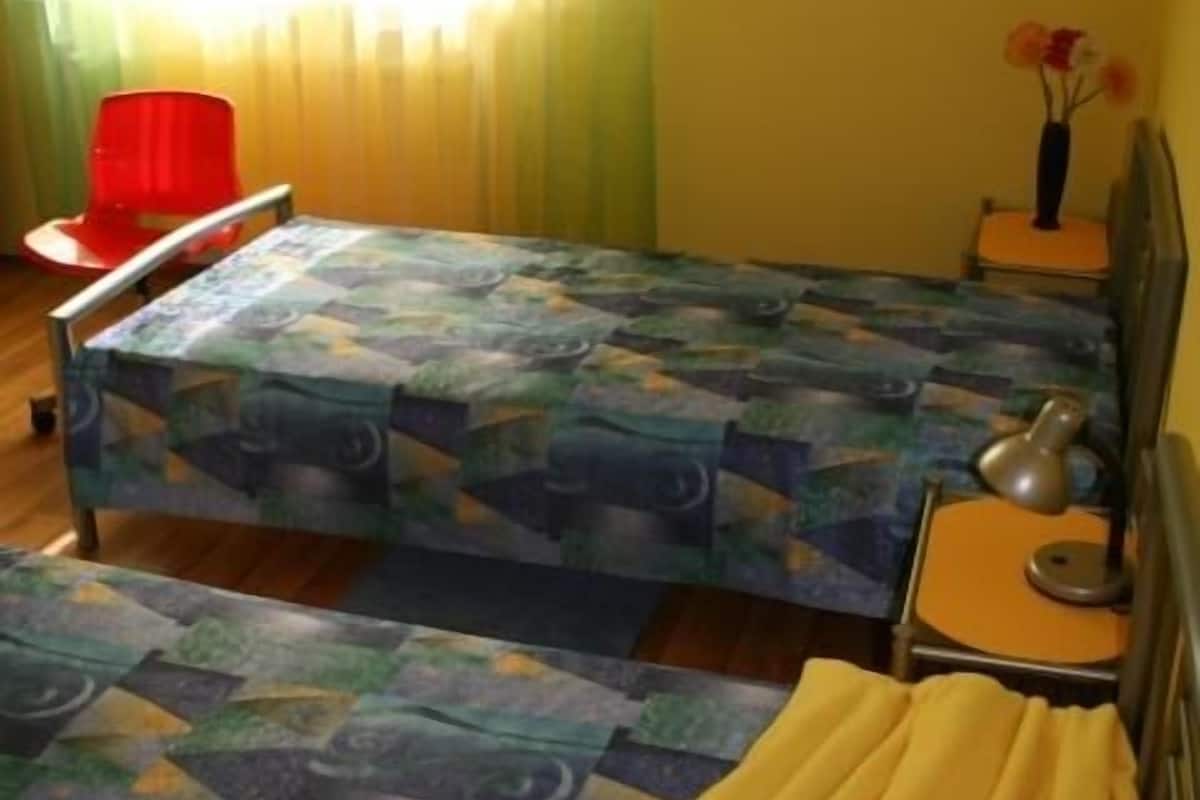Een slaapkamer met een bed, een nachtkastje, een stoel en een raam met gordijnen.