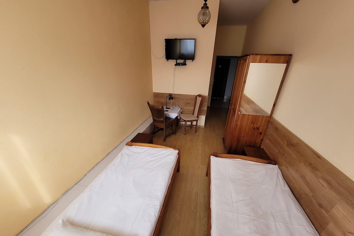 Une chambre d’hôtel avec deux lits simples, un bureau avec une chaise, un téléviseur fixé au mur et une armoire en bois.