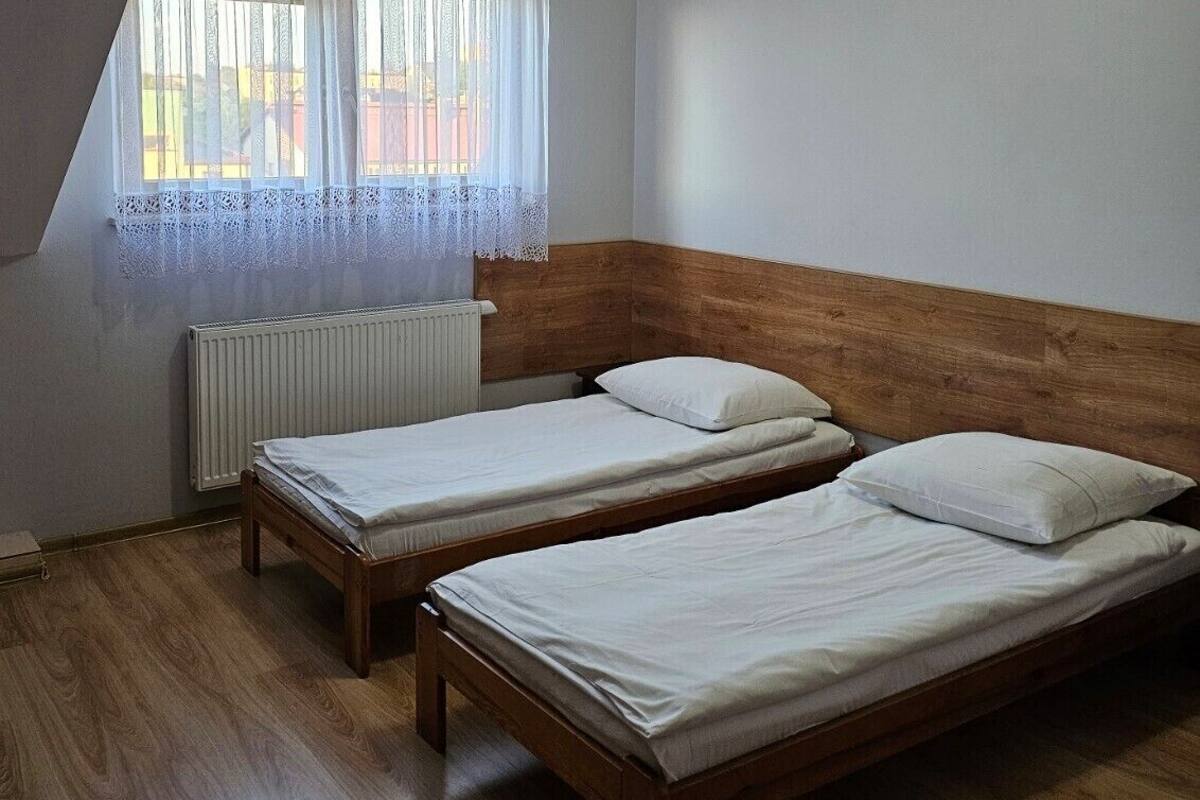 Une chambre avec deux lits en bois, un radiateur et une fenêtre ornée de rideaux en dentelle.