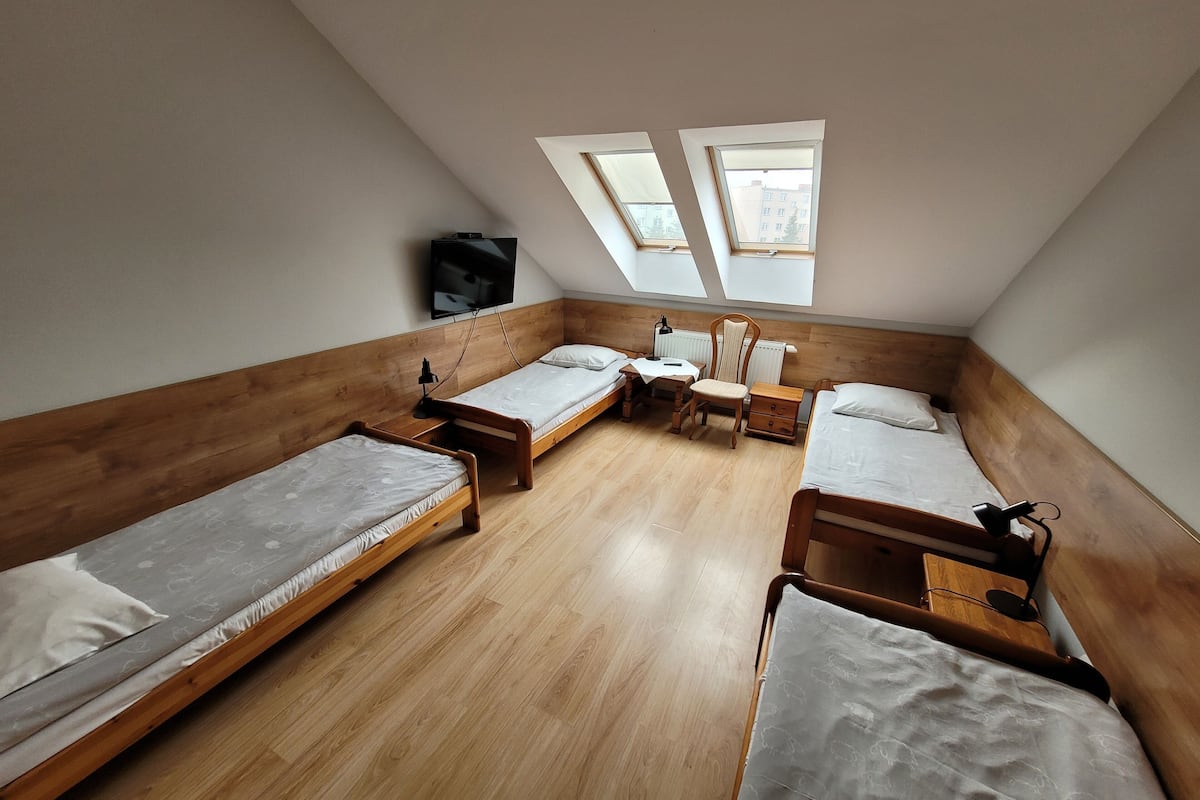 Une chambre de dortoir équipée de quatre lits superposés en bois, d’un bureau, d’une chaise et d’un téléviseur fixé au mur.