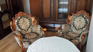 Una habitación con dos sillones ornamentados, un aparador de madera y una mesa redonda con mantel blanco.