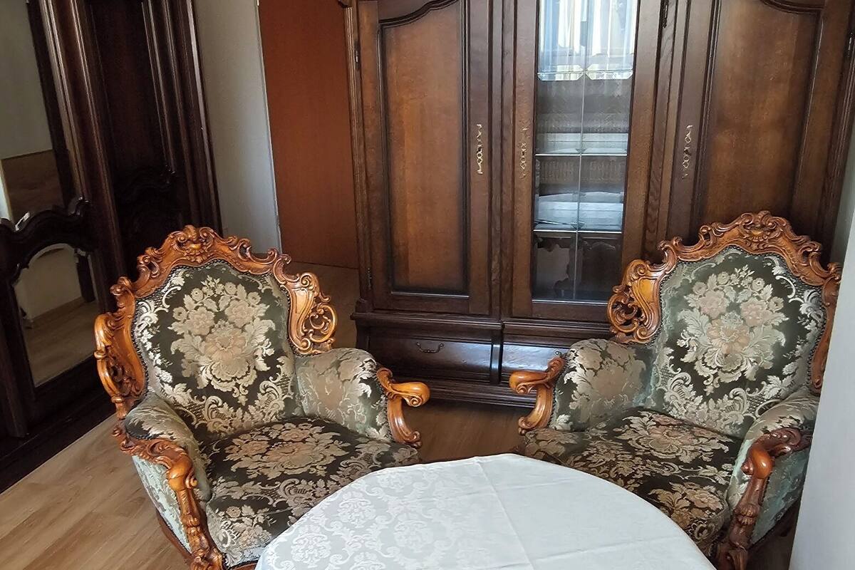 Une pièce comprenant deux fauteuils richement décorés, un buffet en bois et une table ronde recouverte d’une nappe blanche.
